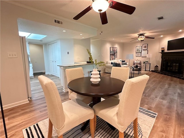 dining room with crown molding, ceiling fan, light hardwood / wood-style floors, and a skylight