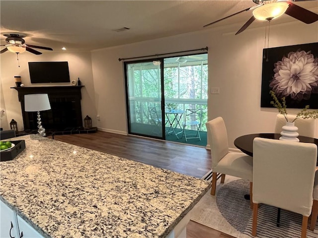 living area with baseboards, visible vents, a fireplace with raised hearth, ceiling fan, and wood finished floors