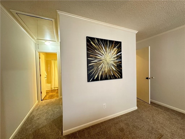 corridor with a textured ceiling, carpet floors, attic access, and crown molding