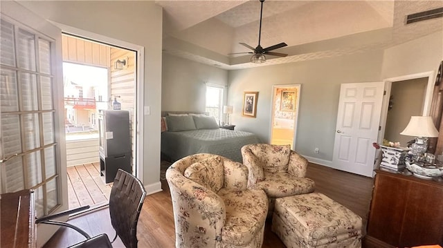 bedroom featuring wood finished floors, visible vents, baseboards, ensuite bathroom, and a raised ceiling