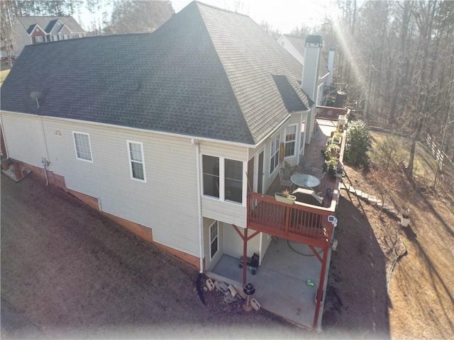 view of side of property featuring a wooden deck, roof with shingles, and a chimney