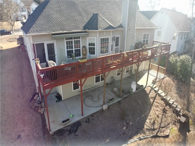 back of house with a patio, a wooden deck, roof with shingles, and a chimney