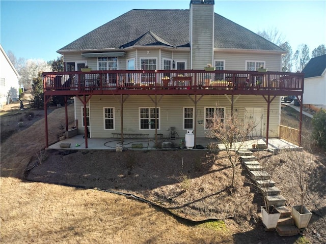 back of house featuring a patio area, a chimney, a shingled roof, and a deck