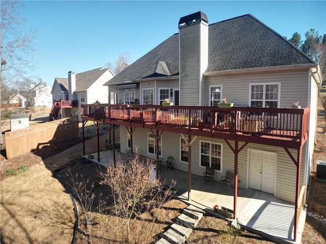 back of property with central air condition unit, a deck, a patio, roof with shingles, and a chimney