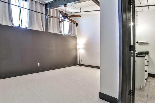 carpeted empty room featuring beamed ceiling, a ceiling fan, and baseboards