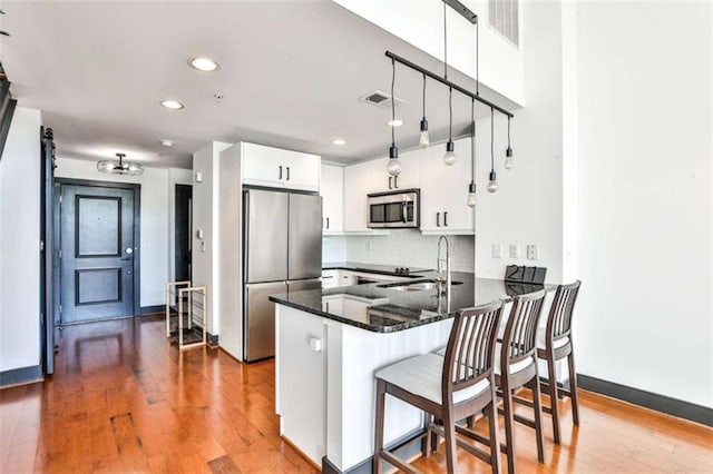 kitchen featuring stainless steel appliances, backsplash, white cabinets, a sink, and a peninsula