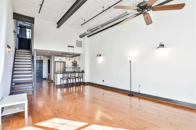 unfurnished living room with hardwood / wood-style flooring, a high ceiling, visible vents, a ceiling fan, and stairs