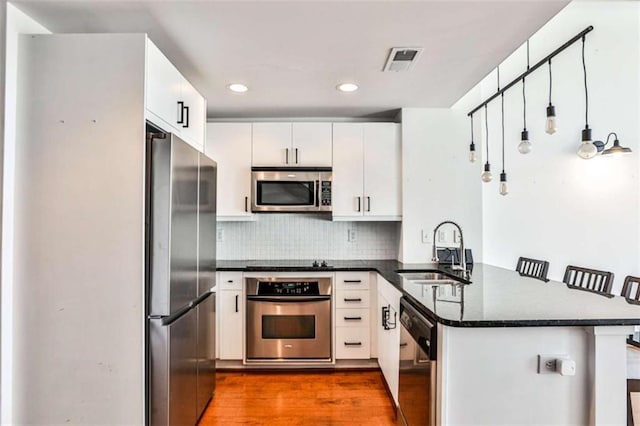 kitchen with visible vents, appliances with stainless steel finishes, wood finished floors, a peninsula, and a sink