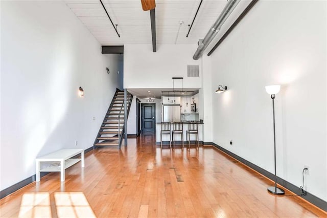 unfurnished living room with baseboards, visible vents, stairway, hardwood / wood-style floors, and beamed ceiling