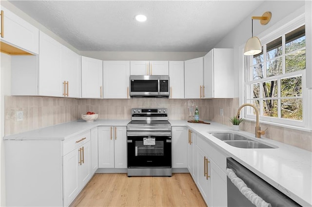 kitchen with tasteful backsplash, stainless steel appliances, light countertops, white cabinetry, and a sink