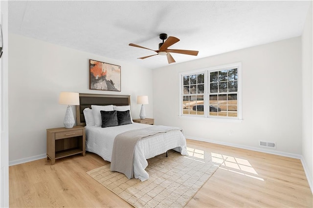 bedroom with a ceiling fan, light wood-type flooring, visible vents, and baseboards