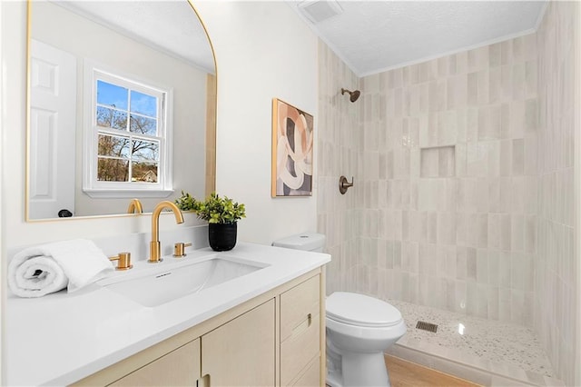 full bathroom with crown molding, a tile shower, vanity, and toilet