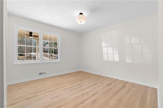 unfurnished room featuring a textured ceiling, wood finished floors, visible vents, and baseboards