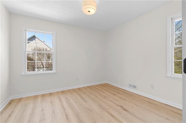 unfurnished room featuring light wood-type flooring, visible vents, and baseboards