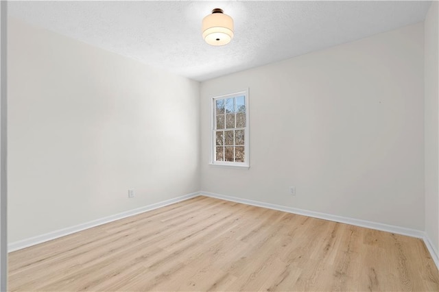 spare room featuring light wood-type flooring, a textured ceiling, and baseboards