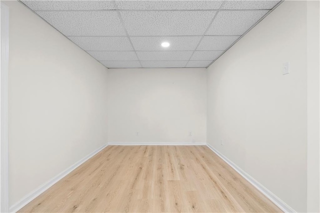 empty room with light wood finished floors, a drop ceiling, and baseboards