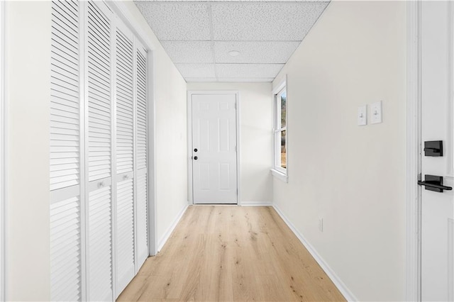 corridor featuring light wood-type flooring, baseboards, and a drop ceiling