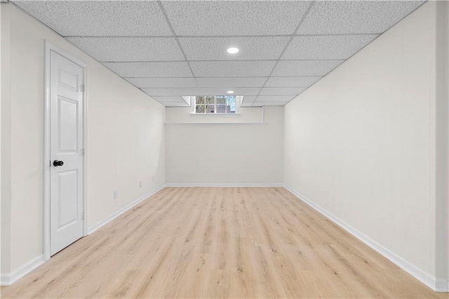 basement featuring a paneled ceiling, baseboards, and wood finished floors