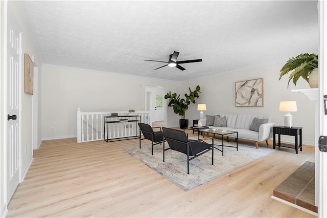 living area featuring ceiling fan, a textured ceiling, baseboards, and wood finished floors