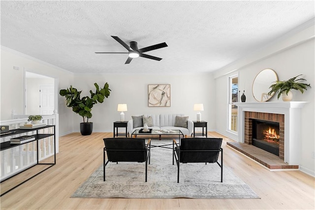 living area with a textured ceiling, ceiling fan, a fireplace, and wood finished floors