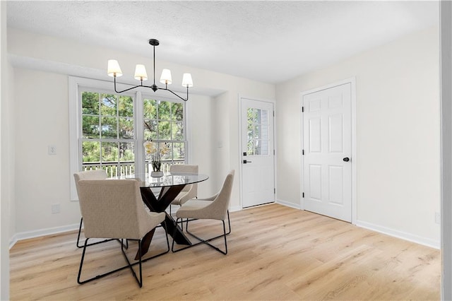 dining area featuring light wood-style floors, a textured ceiling, baseboards, and an inviting chandelier