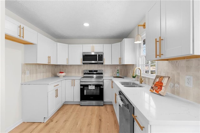 kitchen featuring tasteful backsplash, appliances with stainless steel finishes, white cabinets, a sink, and light wood-type flooring