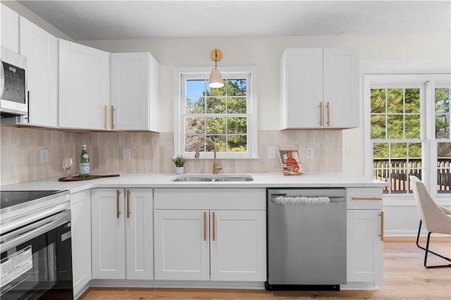 kitchen with appliances with stainless steel finishes, white cabinets, light countertops, and a sink