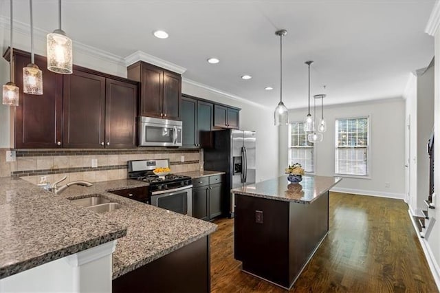 kitchen with sink, stainless steel appliances, a center island, light stone counters, and decorative light fixtures