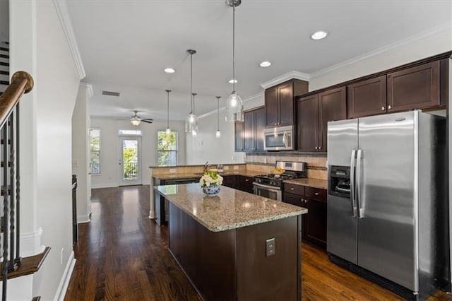 kitchen with dark brown cabinetry, light stone counters, hanging light fixtures, appliances with stainless steel finishes, and kitchen peninsula