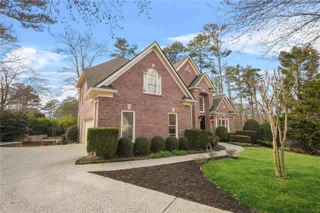 traditional-style home featuring a garage, brick siding, a shingled roof, driveway, and a front yard