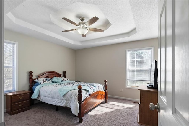 bedroom with a textured ceiling, light colored carpet, a ceiling fan, baseboards, and a tray ceiling