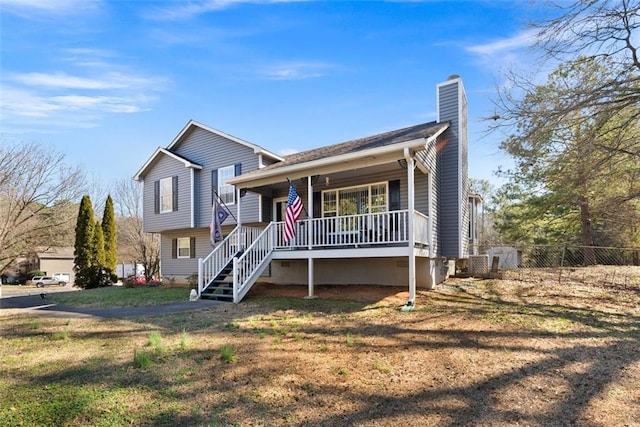 tri-level home with a chimney, covered porch, stairway, a front yard, and fence