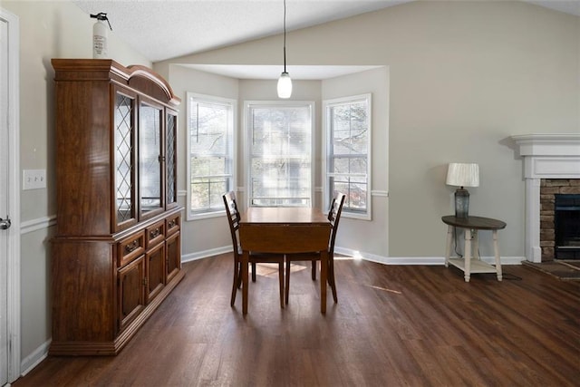 dining area featuring dark wood-style floors, a fireplace, baseboards, and vaulted ceiling