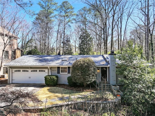 single story home with brick siding, a chimney, a shingled roof, an attached garage, and driveway