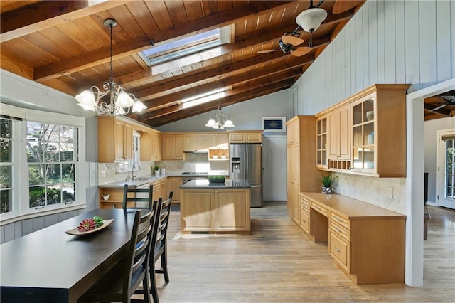 kitchen featuring a notable chandelier, tasteful backsplash, lofted ceiling with skylight, a sink, and stainless steel fridge