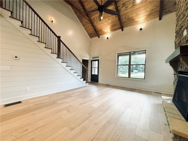 unfurnished living room with wood ceiling, ceiling fan, beam ceiling, light hardwood / wood-style floors, and a stone fireplace