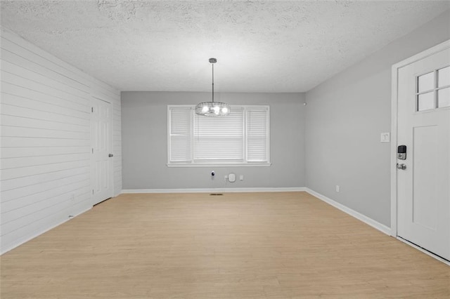 unfurnished dining area with light hardwood / wood-style floors, a healthy amount of sunlight, a textured ceiling, and an inviting chandelier