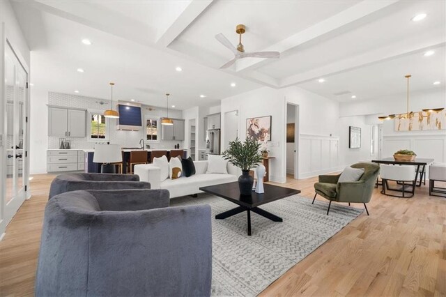 living room with beam ceiling, light hardwood / wood-style flooring, and ceiling fan with notable chandelier