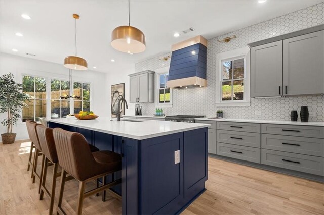 kitchen featuring an island with sink, premium range hood, sink, gray cabinets, and decorative light fixtures