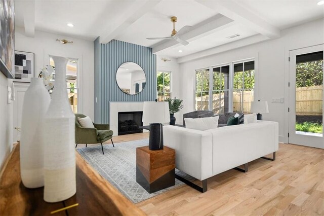 living room with a wealth of natural light, beamed ceiling, light hardwood / wood-style flooring, and ceiling fan