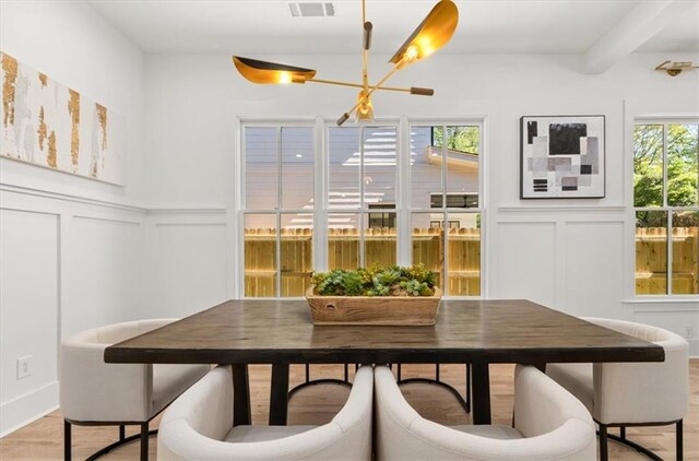 dining space featuring a notable chandelier, beamed ceiling, and light hardwood / wood-style flooring