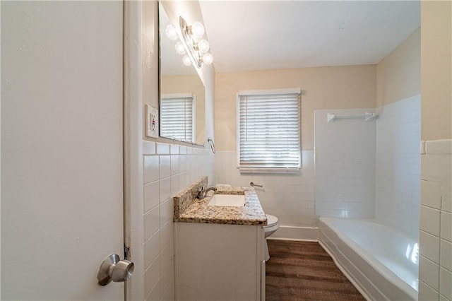 bathroom featuring toilet, a wainscoted wall, wood finished floors, vanity, and tile walls