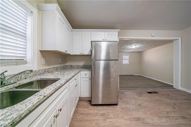 kitchen featuring visible vents, light wood-style flooring, freestanding refrigerator, white cabinetry, and a sink