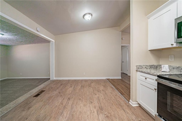 kitchen featuring visible vents, light wood-style flooring, white cabinets, light stone countertops, and range with electric cooktop