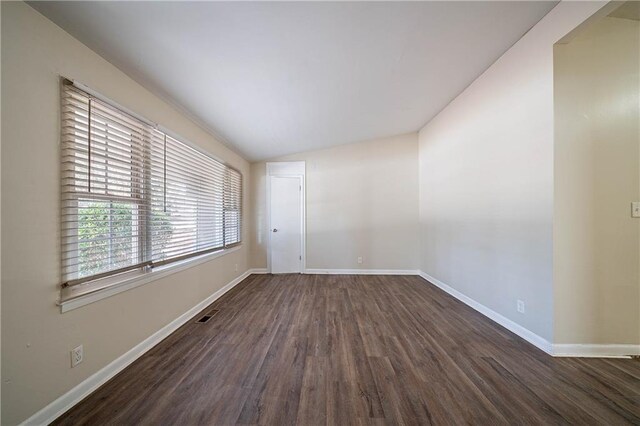 empty room featuring lofted ceiling, dark wood-style flooring, visible vents, and baseboards