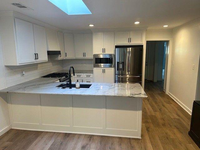 1360 Bethany Ct, Alpharetta, GA 30004 - kitchen featuring stainless steel appliances, a skylight, a peninsula, light stone counters, and recessed lighting