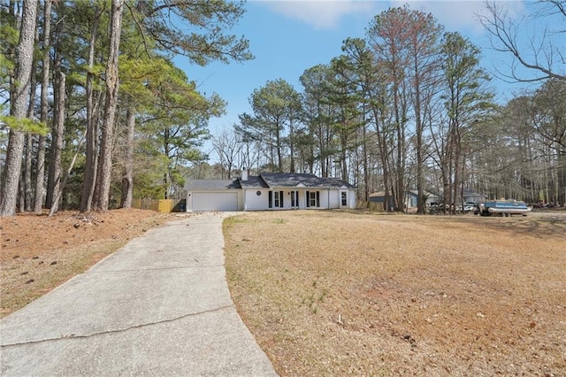 single story home featuring a chimney, an attached garage, concrete driveway, and a front yard