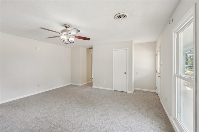 carpeted empty room with visible vents, baseboards, a textured ceiling, and ceiling fan