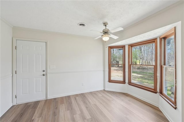 empty room featuring baseboards, visible vents, ornamental molding, a textured ceiling, and light wood-type flooring