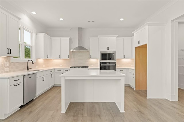 kitchen featuring white cabinets, appliances with stainless steel finishes, sink, wall chimney range hood, and a kitchen island